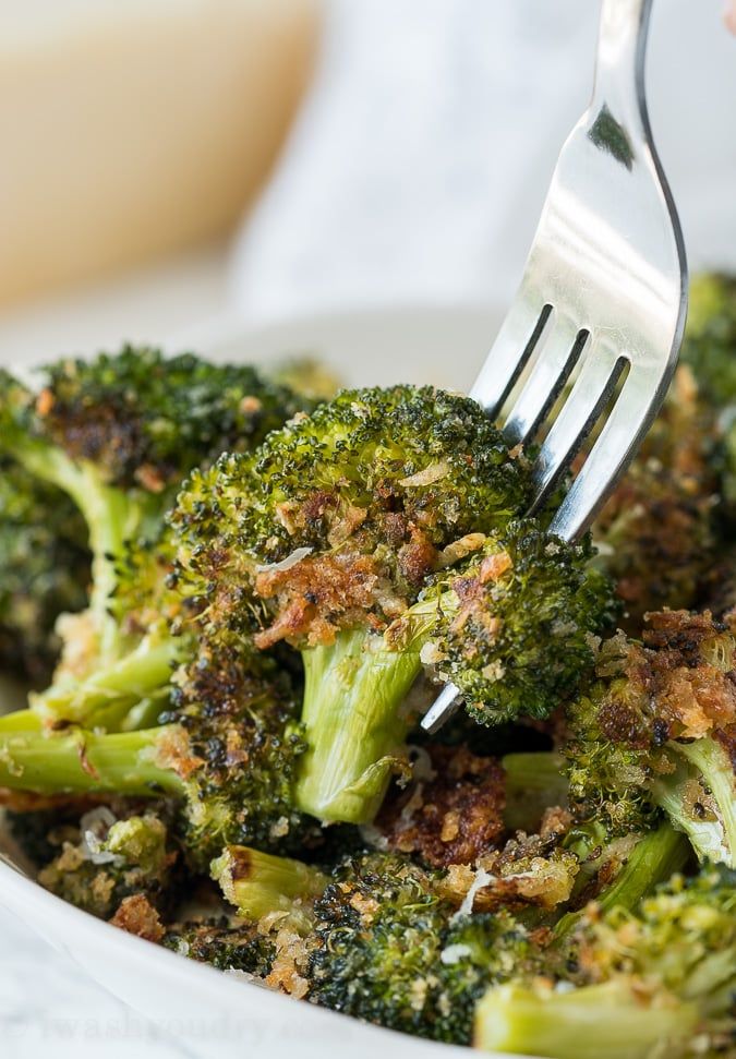 a fork with some broccoli in it on top of a white bowl filled with food