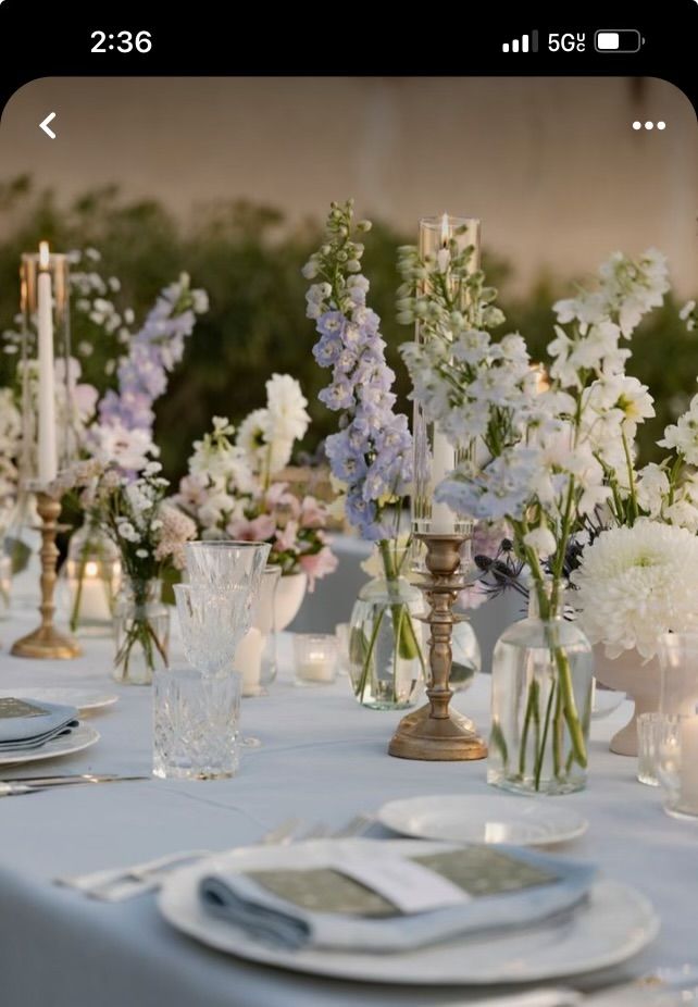 the table is set with white and blue flowers in vases, silverware, and candles