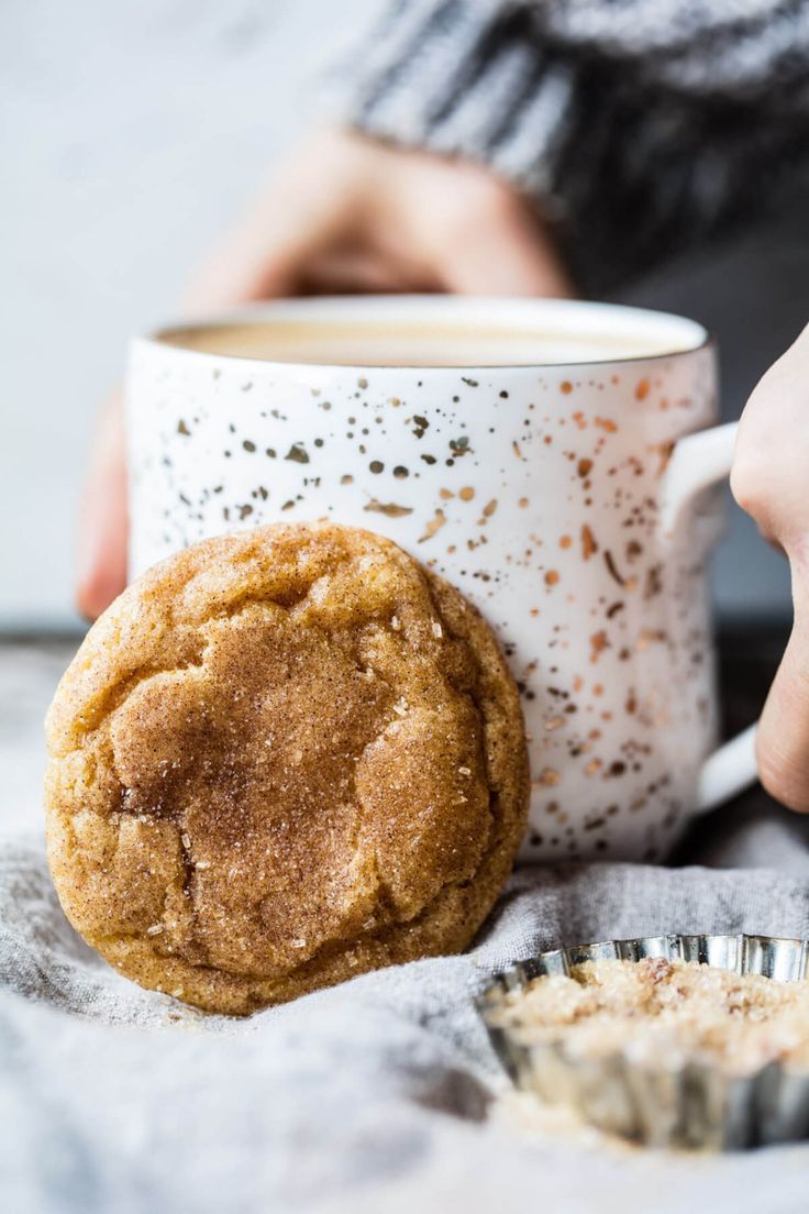 a person is holding a cookie next to a cup of coffee and a muffin