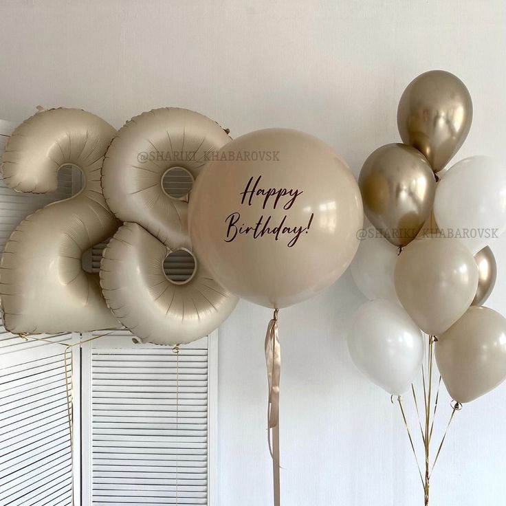 balloons with happy birthday written on them are in front of a white wall and window