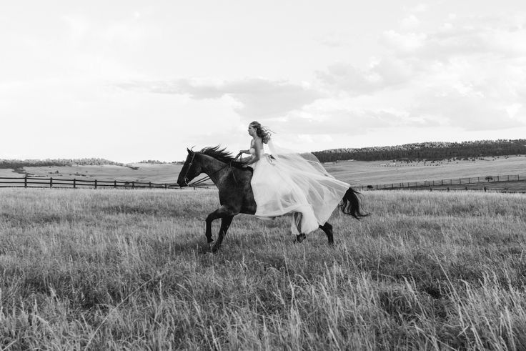 a woman riding on the back of a black and white horse in a field with tall grass