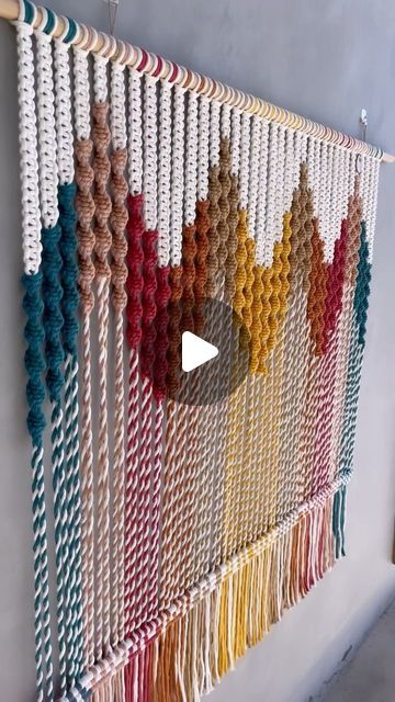 a wall hanging made out of macrame beads and yarn with a video play button