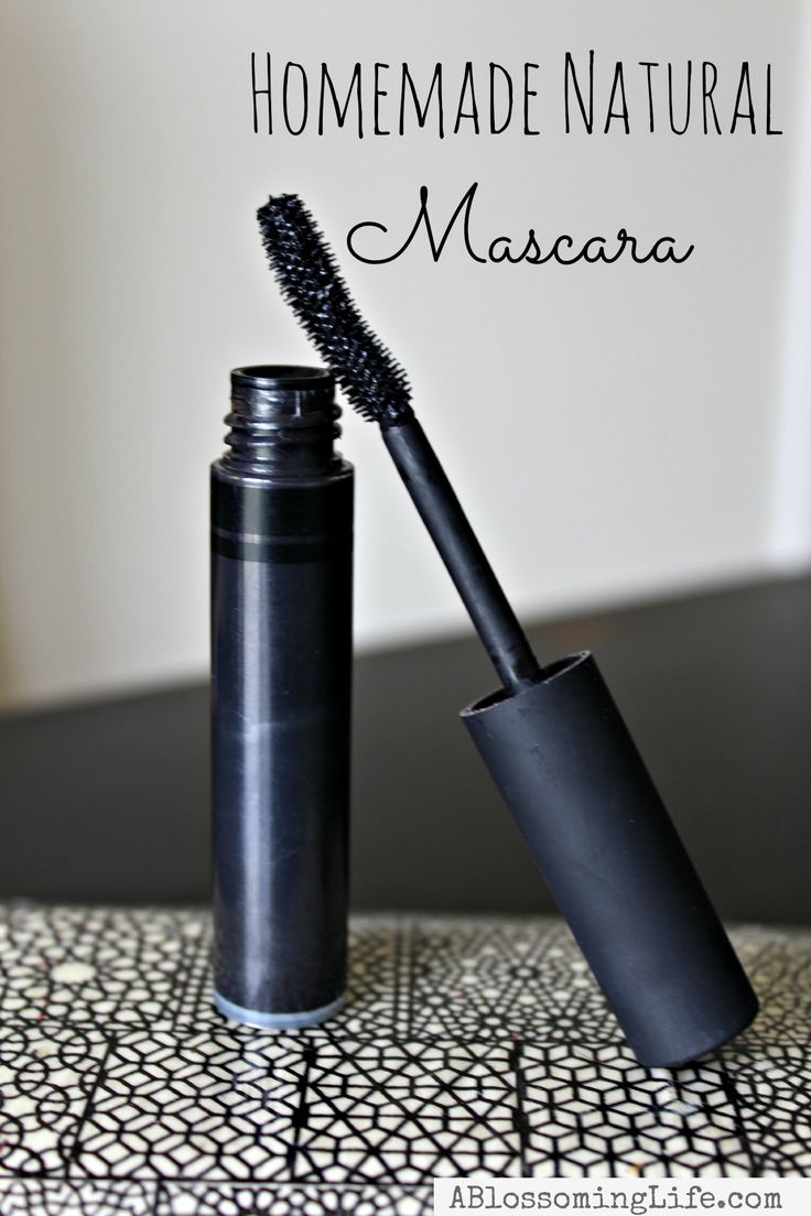 the mascara is black and has a long brush in it's mouth, on top of a patterned tablecloth