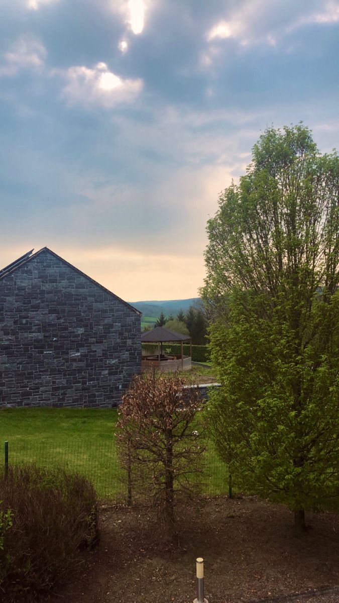 an old barn sits in the middle of a grassy field with trees and bushes around it