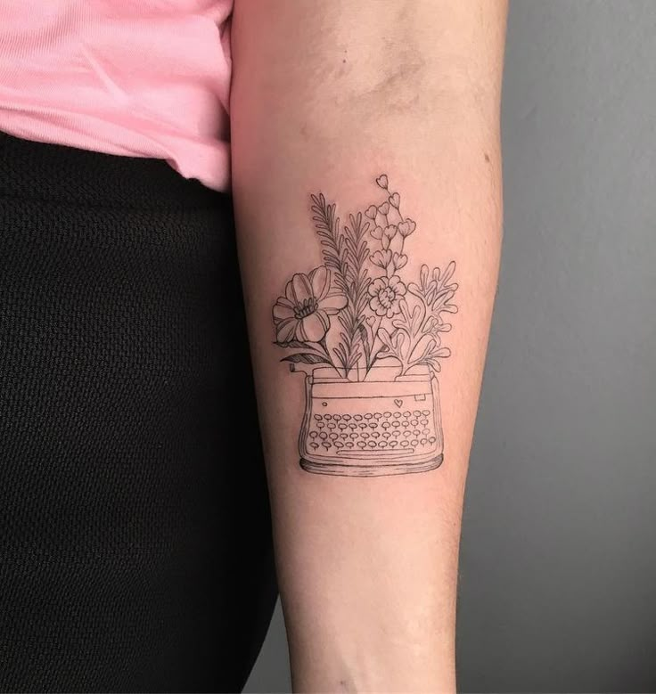 a woman's arm with a flower pot and typewriter tattoo on the left forearm