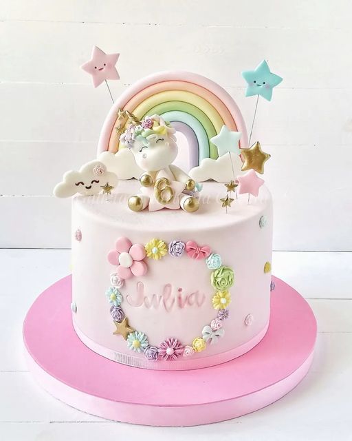 a pink cake decorated with unicorns and rainbows on top of a white table