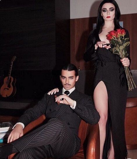 a man sitting on a chair next to a woman in a black dress holding flowers