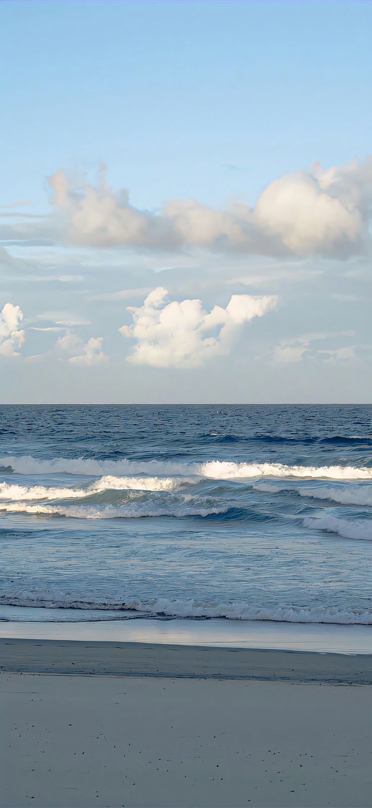 a person walking on the beach with a surfboard in hand and clouds in the background