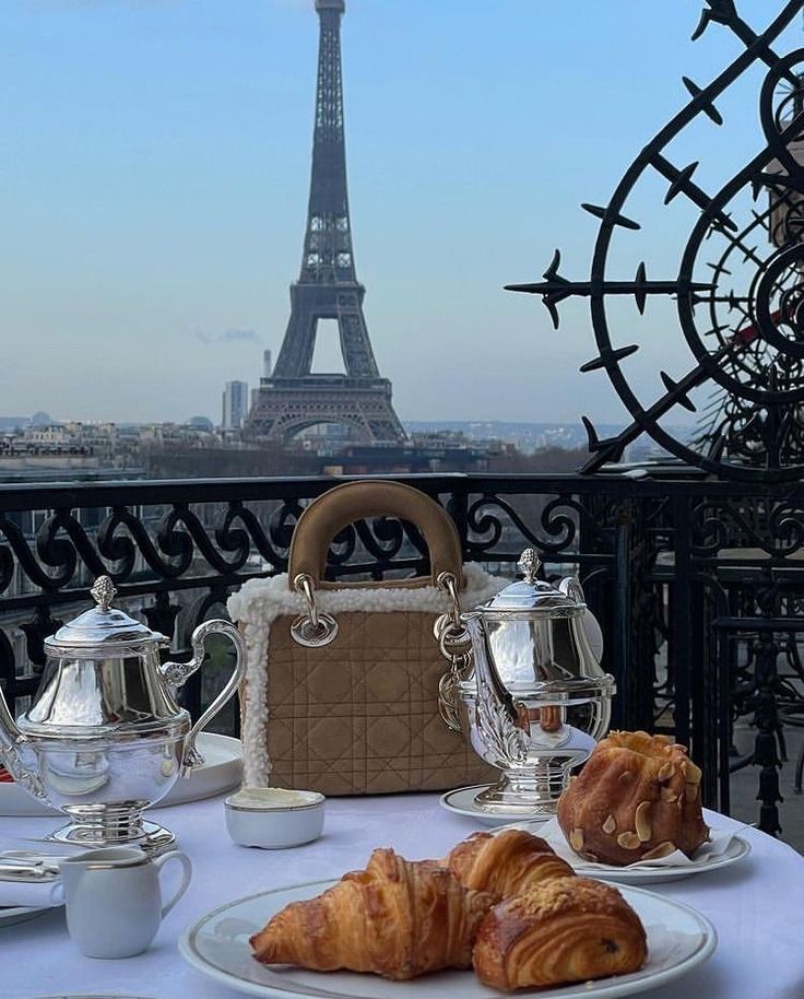 the table is set for breakfast in front of the eiffel tower, with coffee and croissants on it