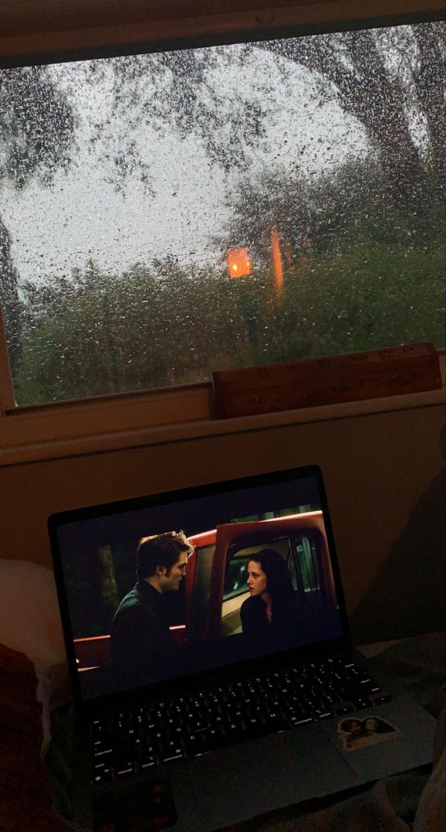 a laptop computer sitting on top of a desk next to a window covered in rain