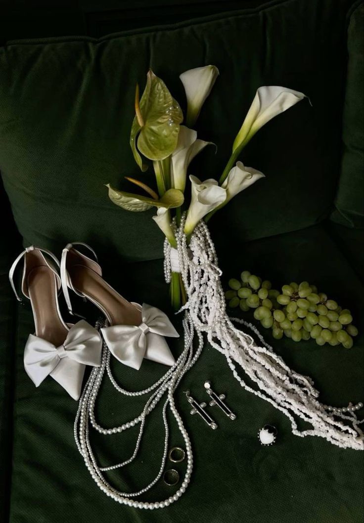 wedding shoes, pearls and flowers on a green couch next to the bride's accessories