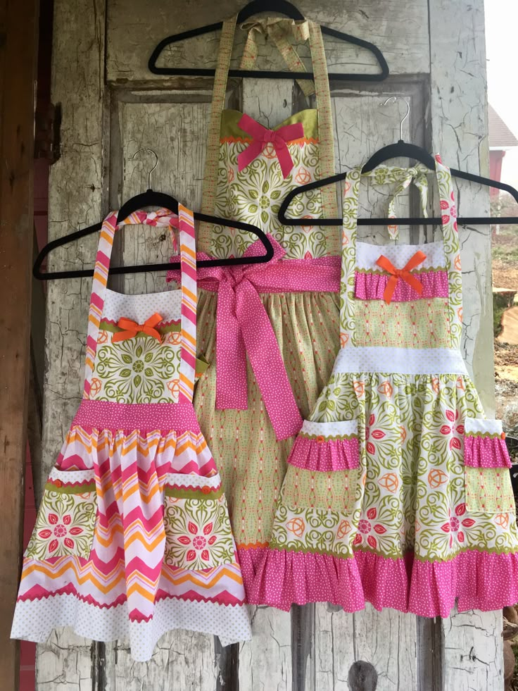 three aprons are hanging on a rack with clothes attached to the hangers in front of an old door