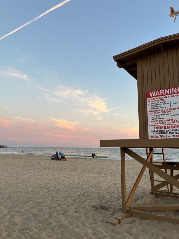 a lifeguard tower on the beach with people in the water and an airplane flying overhead