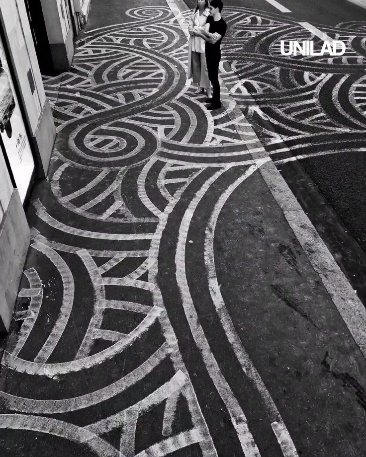 two people are walking down the street with an intricate design on the sidewalk in black and white