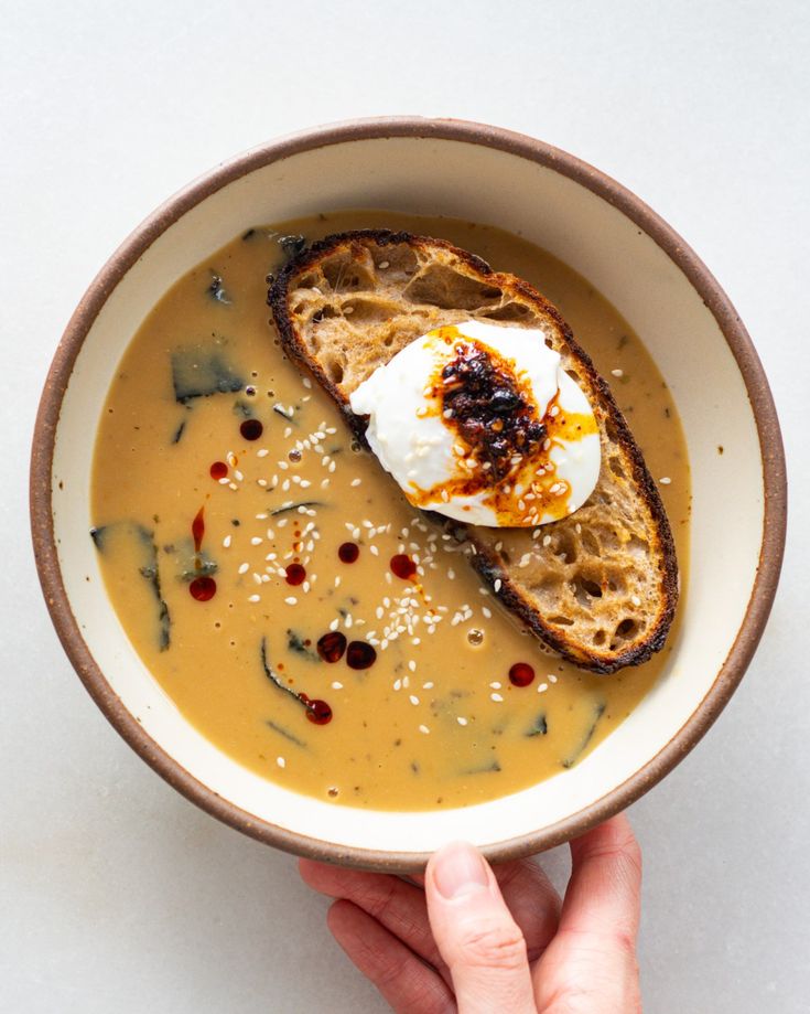 a person is holding a bowl of soup with toast and sour cream on the top