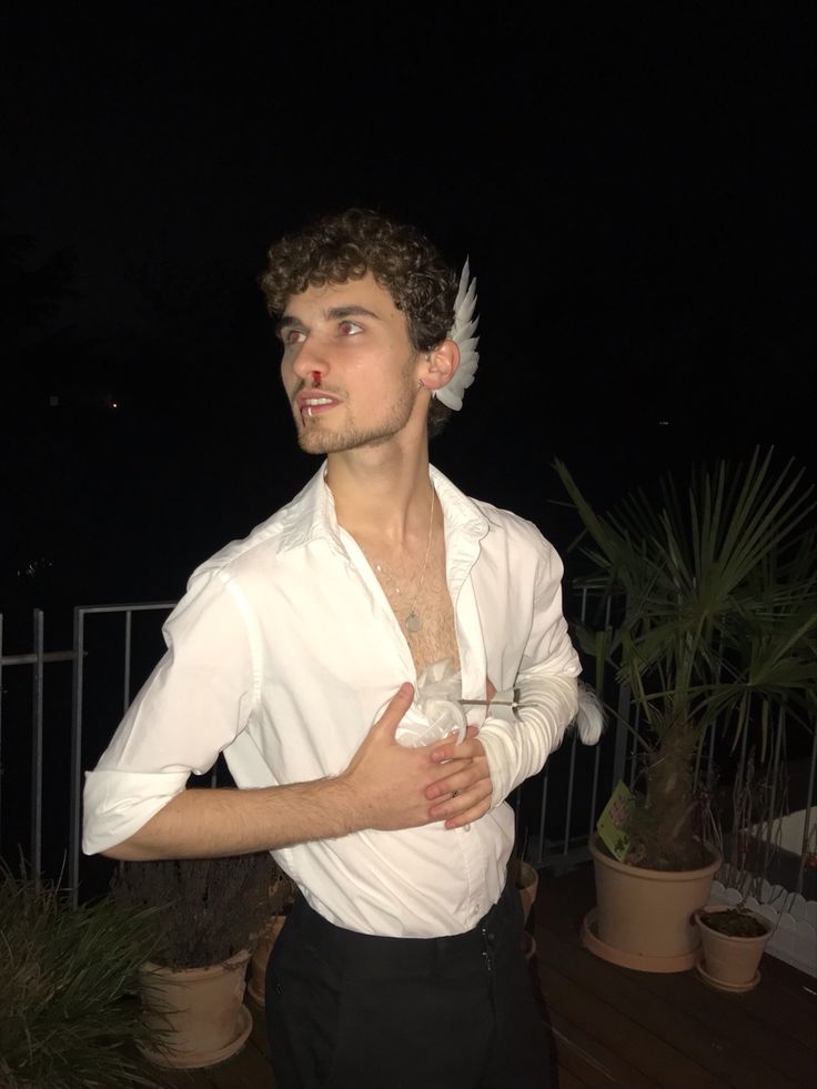 a man in white shirt and black pants standing next to potted plants at night