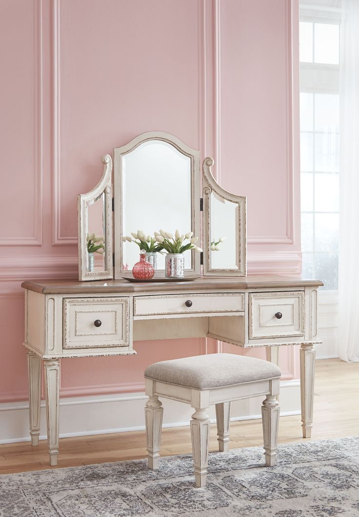 a white dressing table with a mirror and stool in front of a pink painted wall