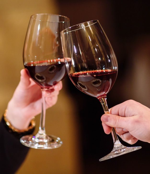 two people holding wine glasses with red wine in them