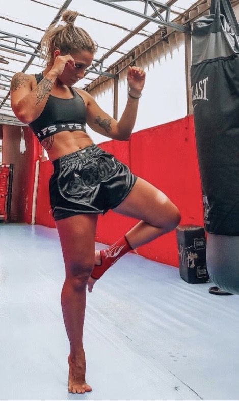 a woman standing in a boxing ring with her leg up and one hand on her head