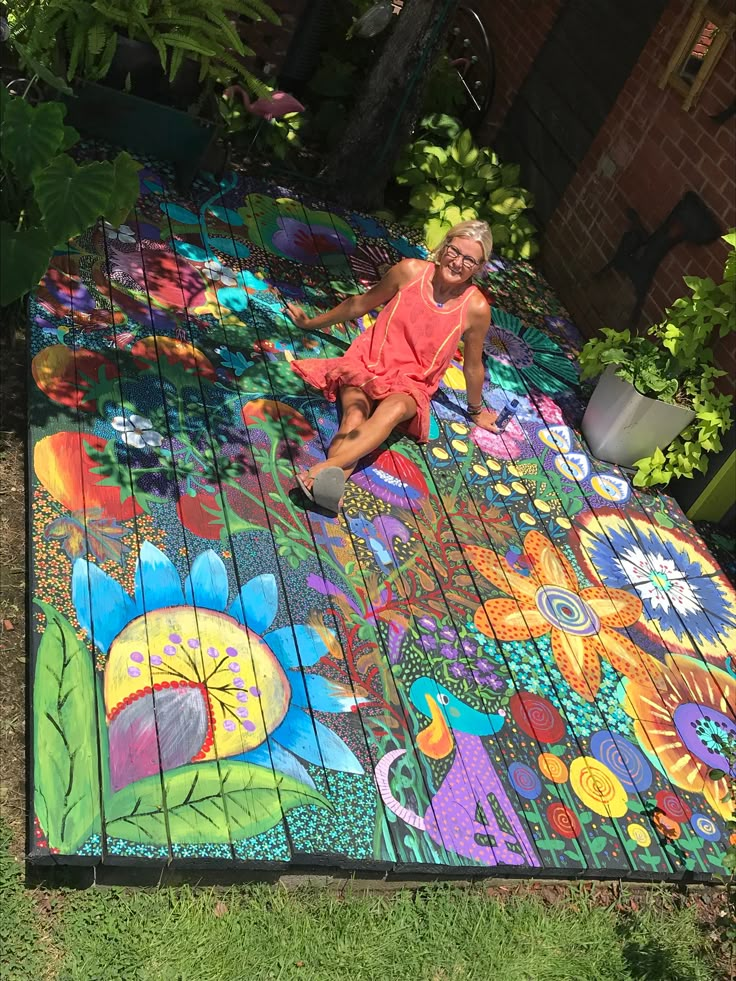 a woman sitting on top of a wooden table covered in colorful flowers and leaves next to potted plants