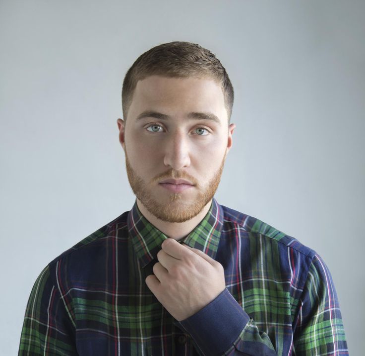 a man with a beard is looking at the camera and has his hand on his tie