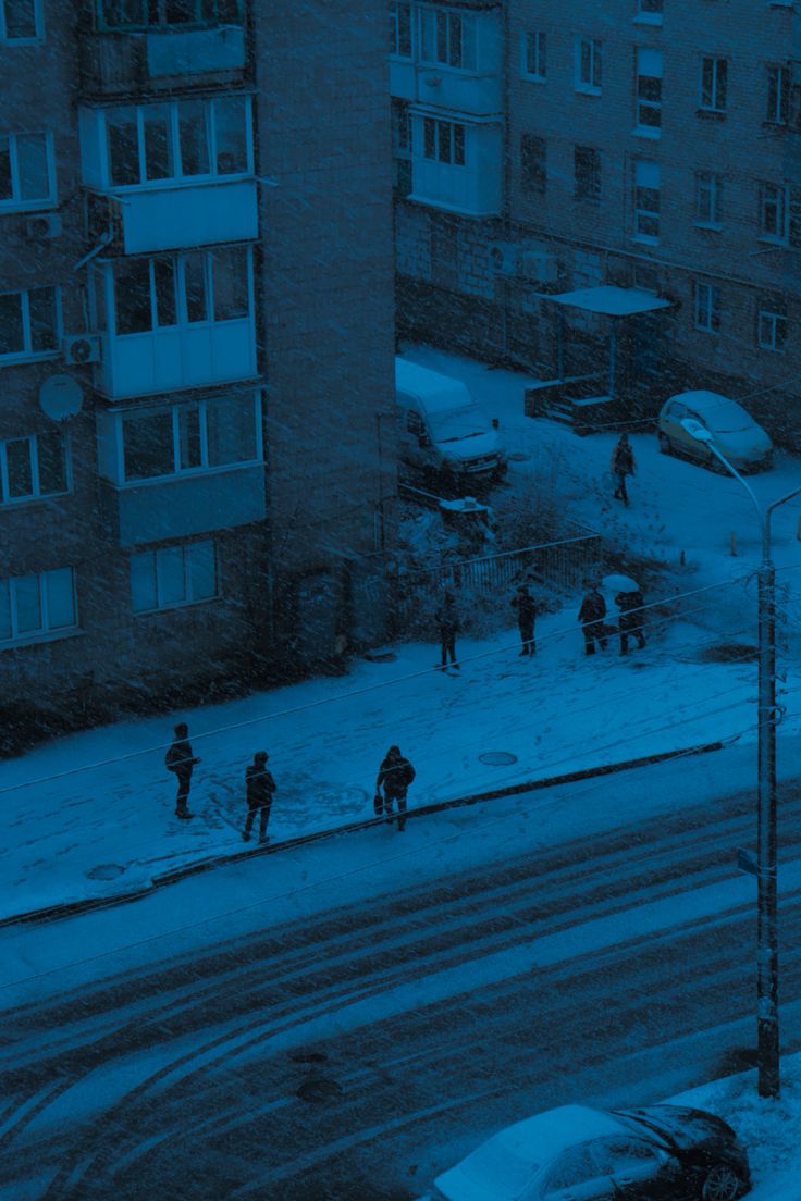 some people are walking in the snow on a city street with cars and buildings behind them