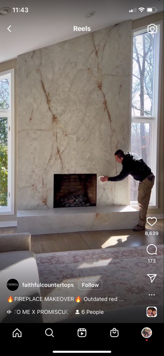 a man standing in front of a fire place next to a large white wall with windows