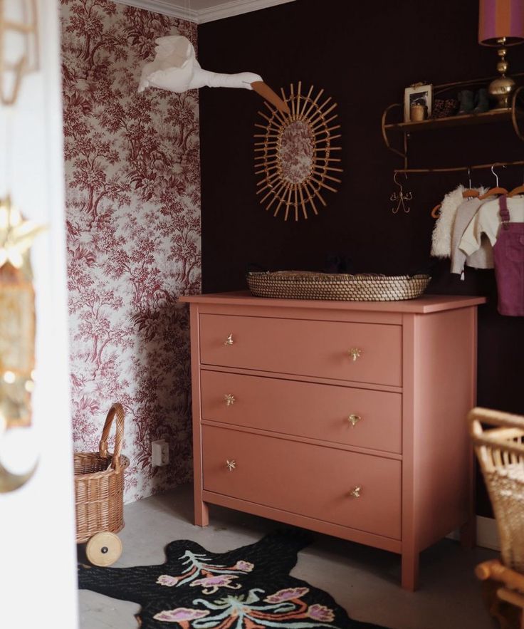 a pink dresser in a room with red wallpaper and gold accessories on the shelves