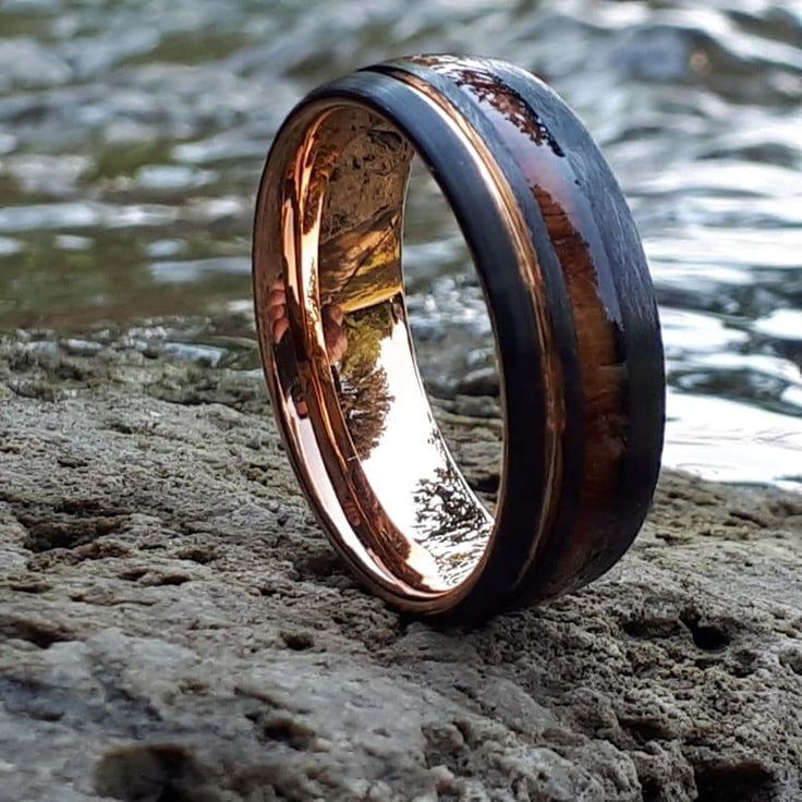 a wedding ring with wood inlays on top of a rock by the water