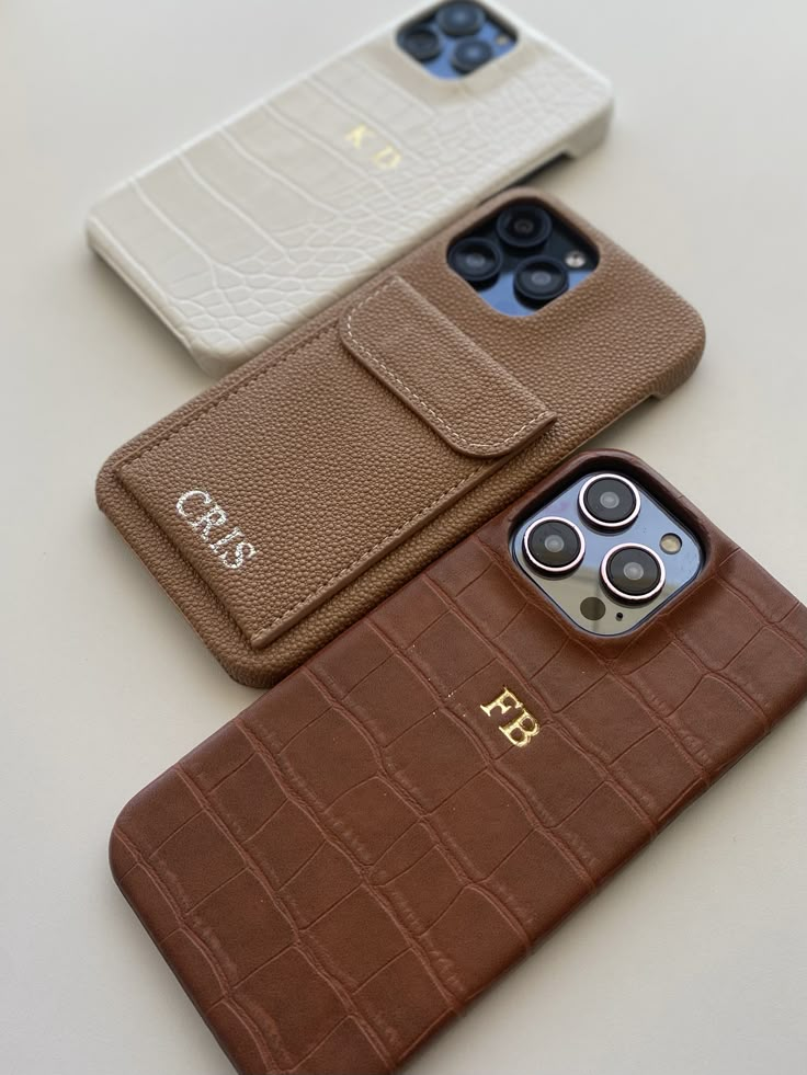 three cell phones sitting next to each other on top of a white table with brown cases