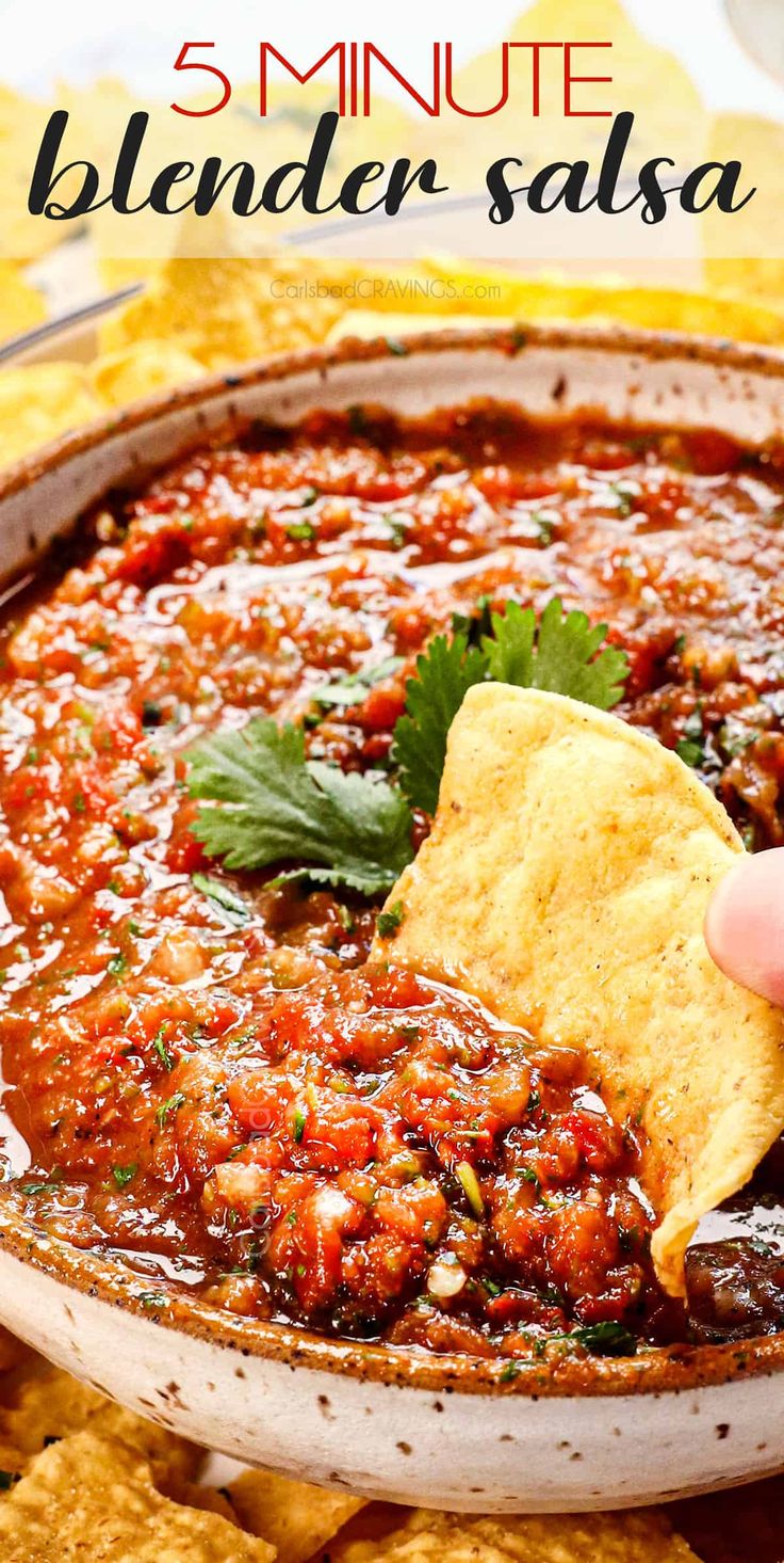 a hand holding a tortilla chip and dipping it into a bowl filled with salsa