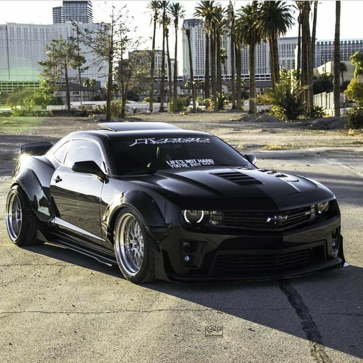 a black sports car parked in front of some palm trees and tall buildings on the other side