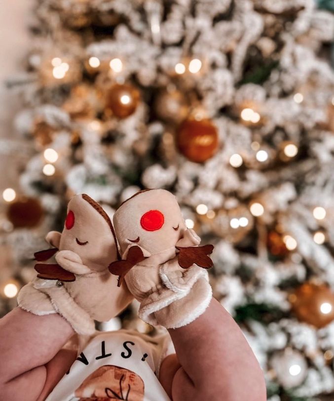 a baby holding two stuffed animals in front of a christmas tree