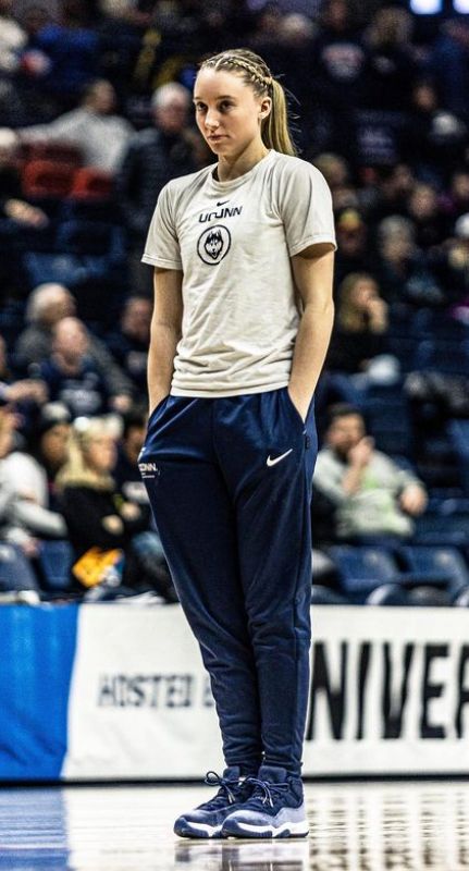 a female basketball player stands on the court in front of an arena full of people