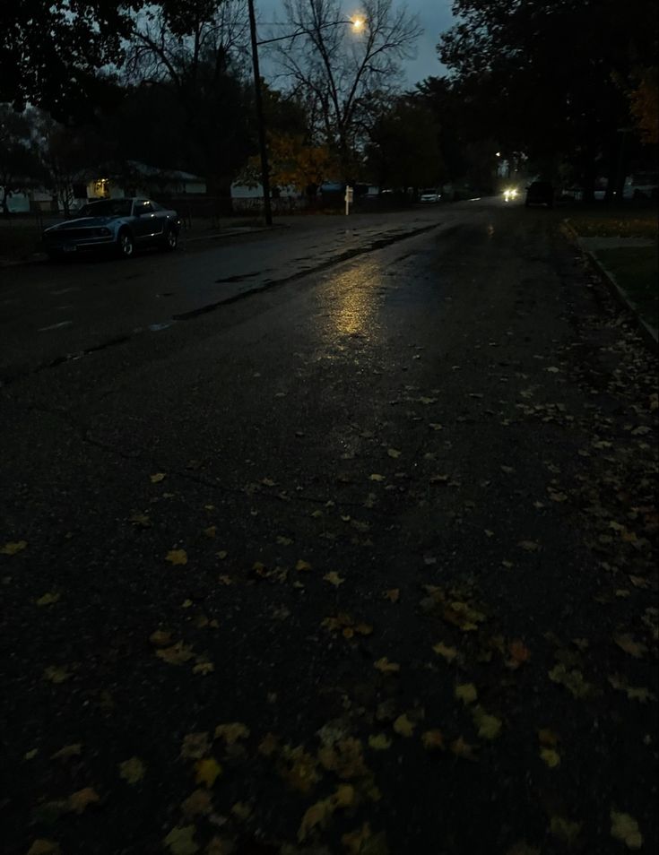 an empty street at night with cars parked on the side and trees in the background