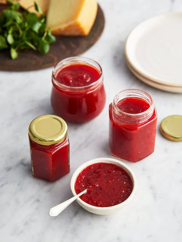 three jars filled with jam sitting on top of a table next to slices of cheese