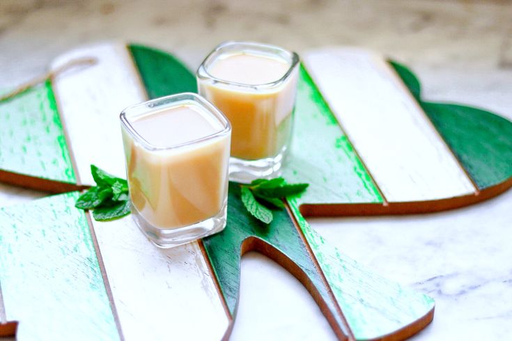 two glasses filled with liquid sitting on top of a green leafy table cloth next to each other