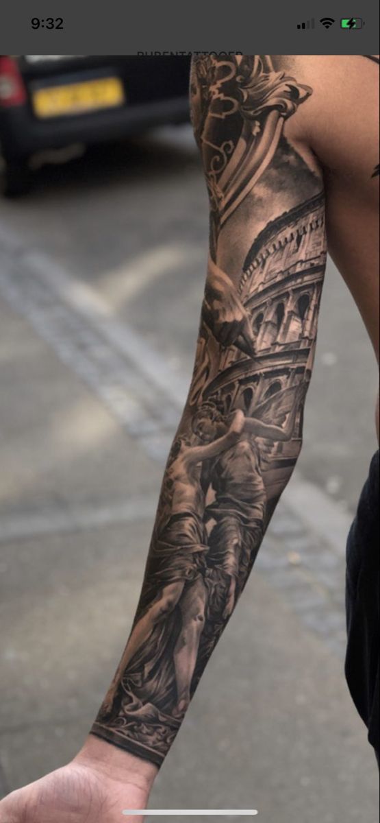 a man's arm with tattoos on it and an image of a statue in the background