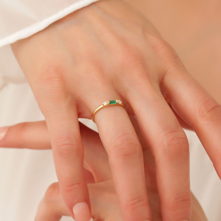 a woman's hand wearing a gold ring with an emerald stone on the middle