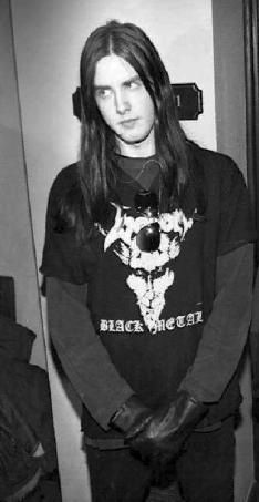 a young man with long hair standing in front of a mirror wearing black leather gloves