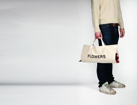 a man holding a bag with flowers on it standing in front of a white background