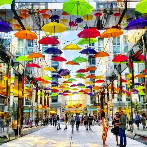 many colorful umbrellas are hanging from the ceiling in an open area with people walking around