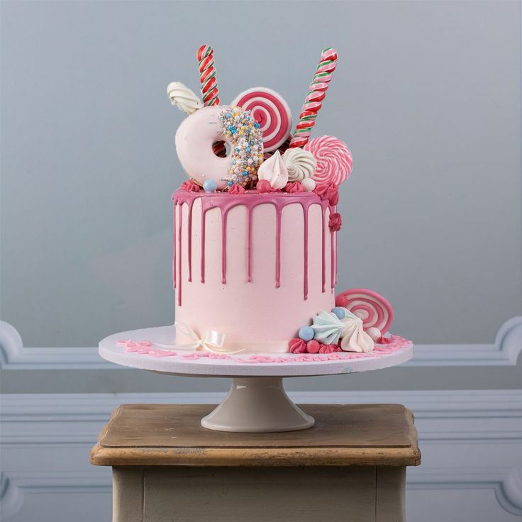 a pink cake decorated with candy and lollipops is on a table in front of a gray wall