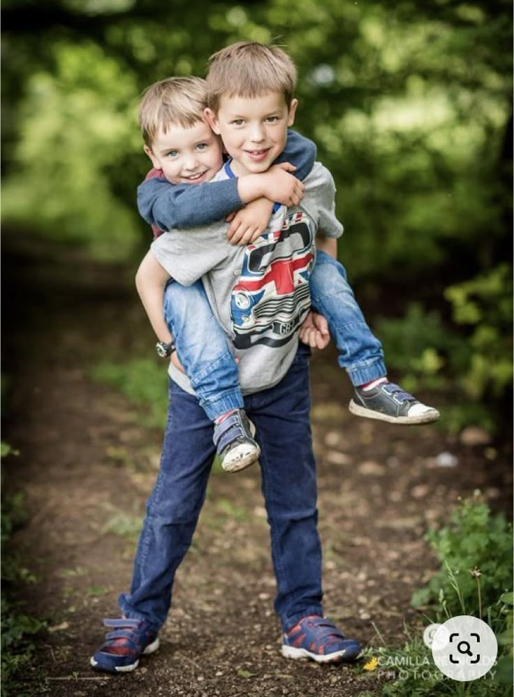 two young boys hugging each other on a dirt path in the middle of some trees