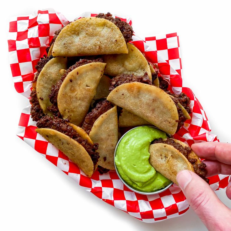 there is a hand holding a taco in the middle of a basket with chips and guacamole