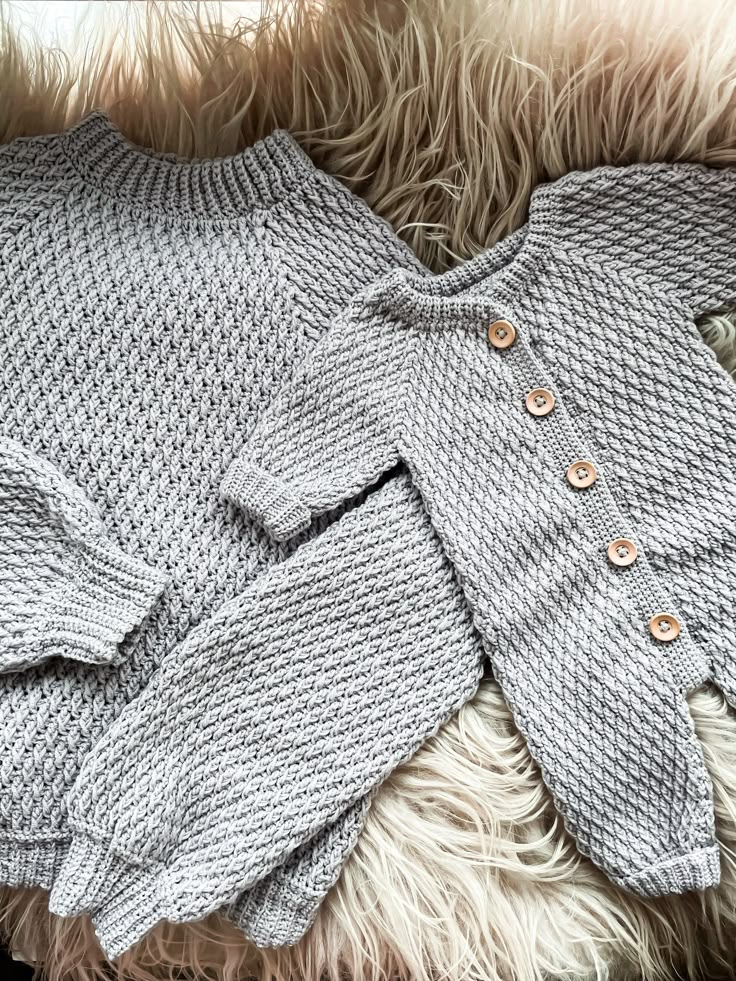 two sweaters laying on top of a fur covered floor next to each other with buttons