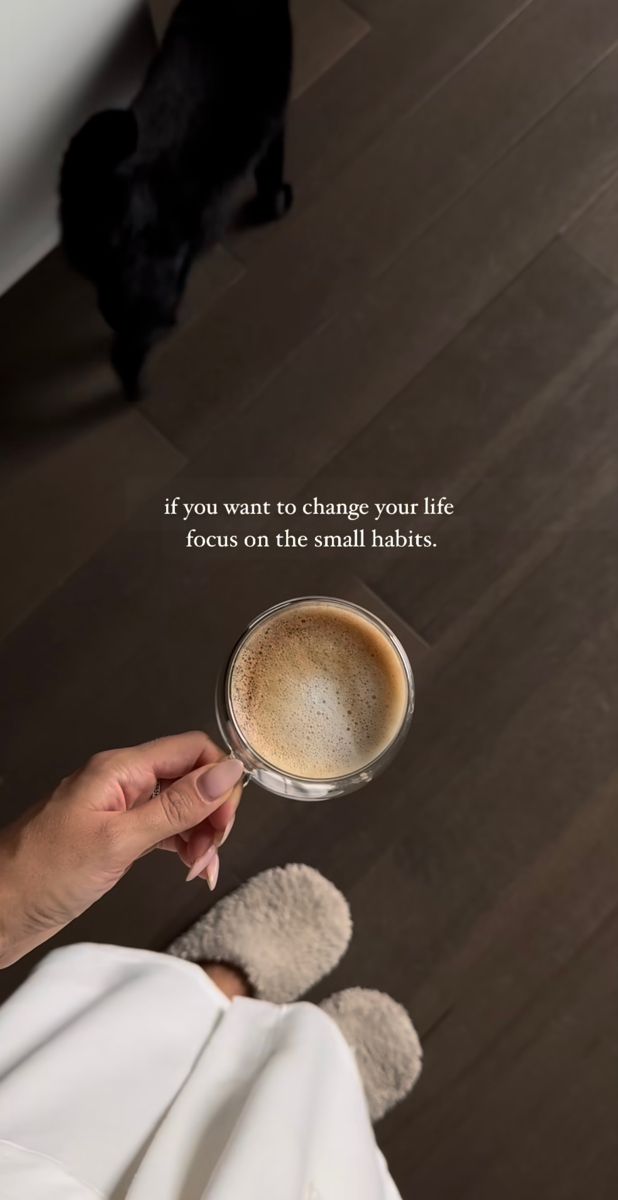 a person holding a cup of coffee in front of a black dog on the floor