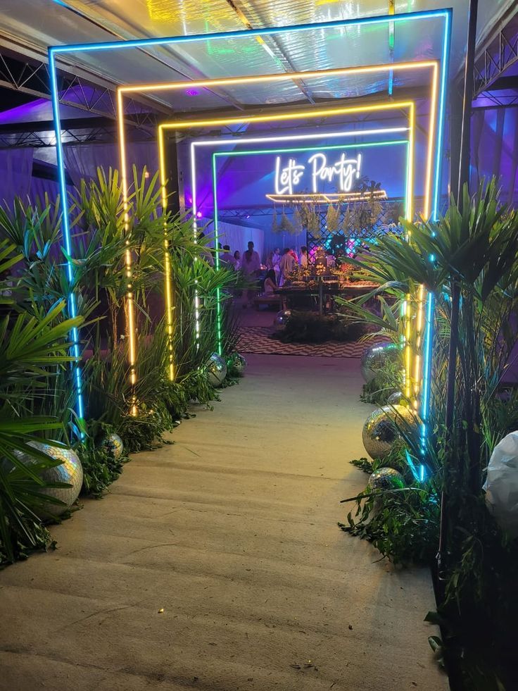 an entrance to a garden with plants and lights on the sides, in front of a building that says let's party