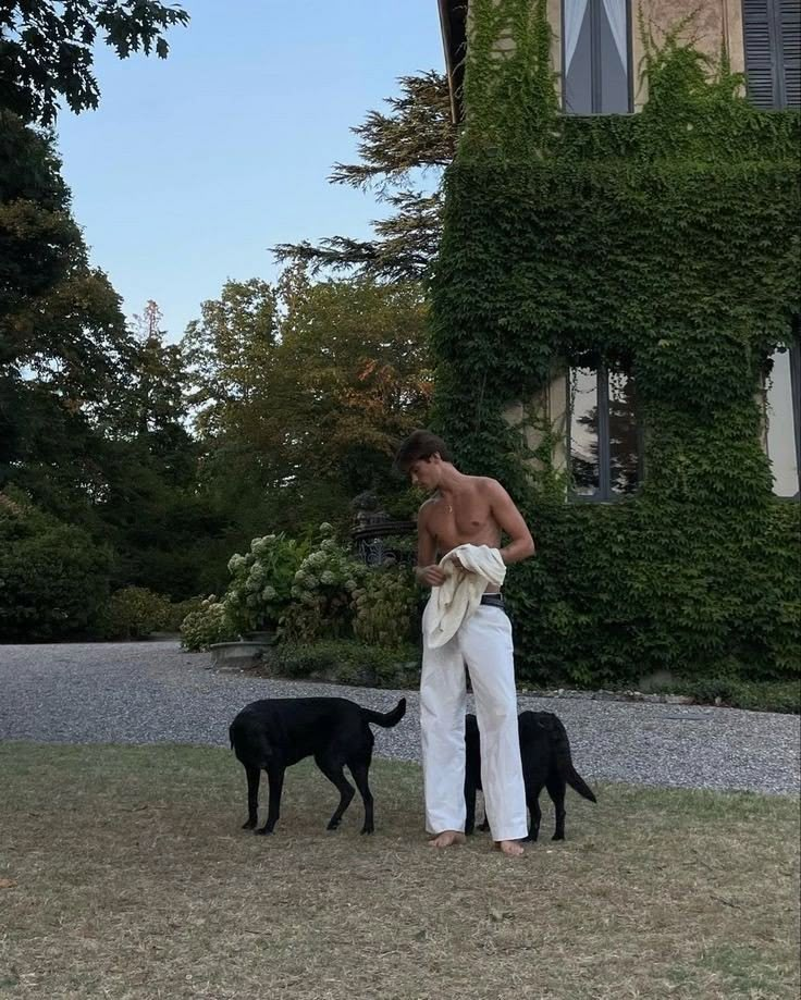 a shirtless man standing next to two black dogs