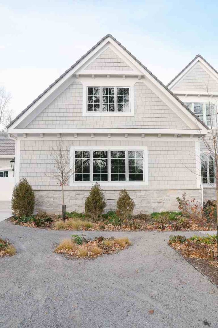 a house with white trim and windows in the front yard, surrounded by shrubs and trees